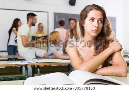 Alone sad student being bullied by a group of students her chin on her hand
