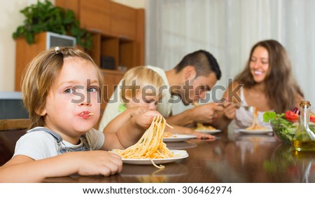 Young happy family of four eating with spaghetti at table. Focus on girl