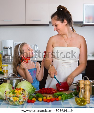 Little girl with mom cutting vegetables for soup at kitchen