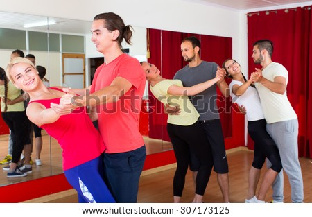 Romantic couple learning to dance tango in dancing school. Two other couples dancing in background