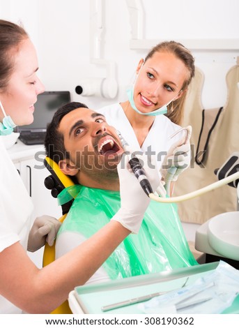 Female dentist with assistant diagnostics the oral cavity of male patient at clinic