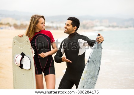Cheerful adult couple running on the beach with surf boards