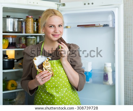 Hungry woman near the opening fridge eating chocolate