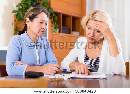 Frustrated senior ladies checking invoices at office.