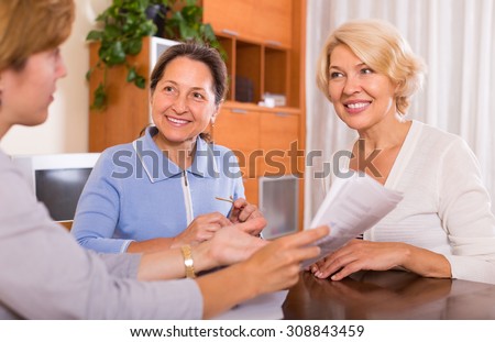 Positive senior ladies signing documents at bank with agent. Focus on brunette