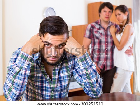 Portrait of unhappy man and loving couple at home: problems of love triangle