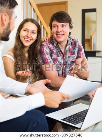 Young happy salesman try hard to sign a contract with merried couple at home