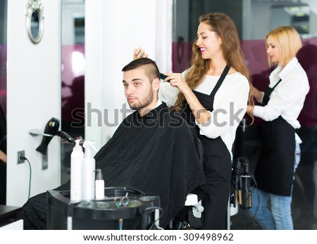 Happy young hairdresser doing hairstyle for young men