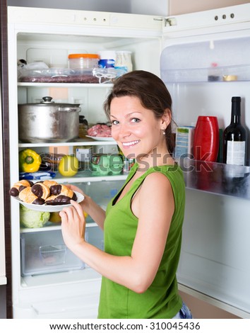 Happy brunette woman eating cake from fridge  at home