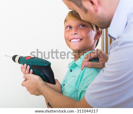 Smiling son helping proud father to drill wall at home