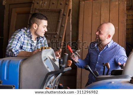 Two happy european mechanics reparing old agrimotors at farm