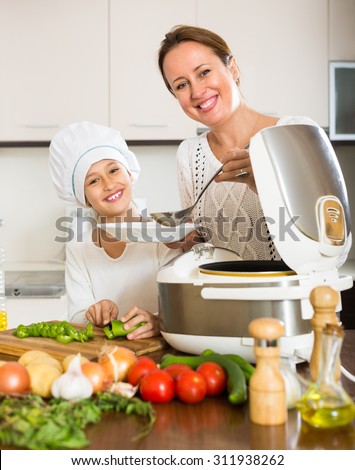 Portrait of smiling little girl and her mom with rice cooker. Focus on woman
