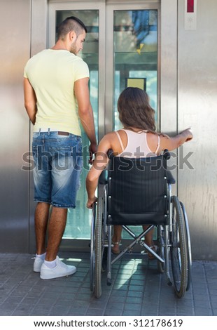 Handsome young man helping handicapped girlfriend at outdoor elevator