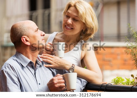 Smiling mature couple discussing and drinking coffee at balcony