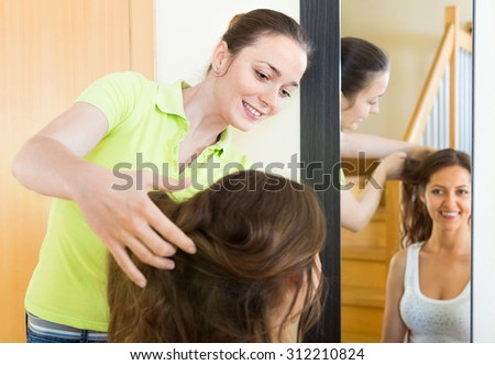 Smiling beautiful girl doing hairstyle for her girlfriend