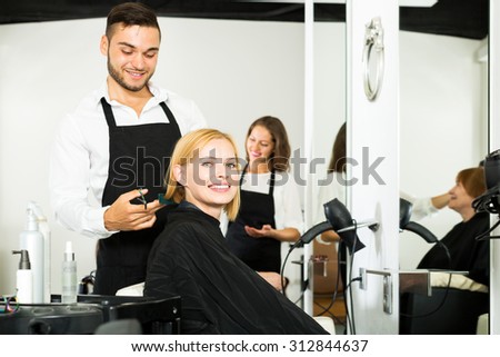 Hair stylist working on haircut for adult beautiful woman. Focus on the woman