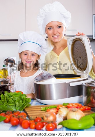 Positive mother and little girl preparing vegetables in slow-cooker