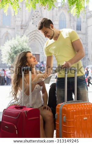 Smiling couple with luggage reading the map at street