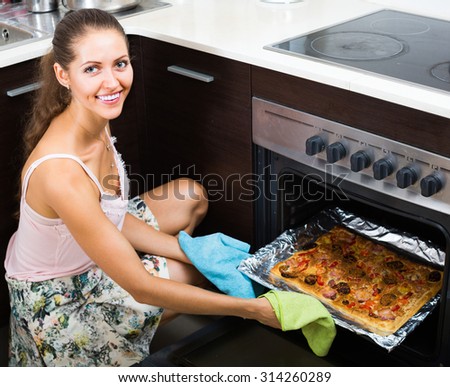 Smiling young housewife pulling tray with homemade pizza out of the oven