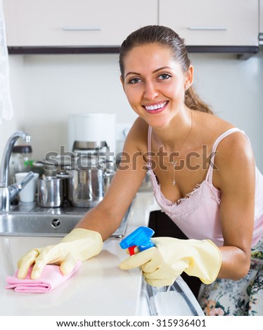 Attractive woman washing kitchen top with detergent