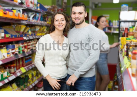 smiling european customers standing near shelves with canned goods at shop