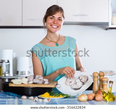 smiling american housewife putting pieces of white fish in tray