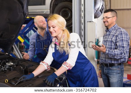 Smiling service crew and satisfied driver standing near car indoor. Focus on woman