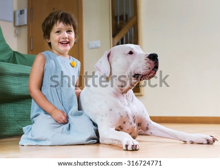 Smiling cute little girl with big white dog lying on the floor at home