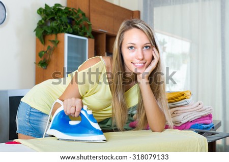 Smiling young blonde woman ironing at ironing board in home