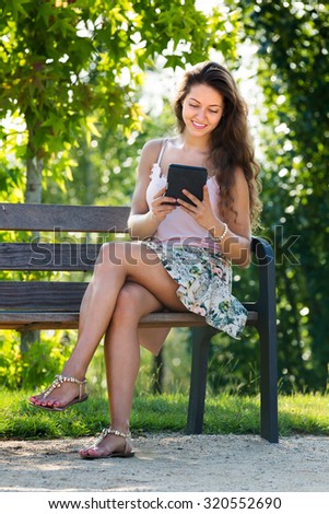 Young woman sitting on bench in park and using tablet