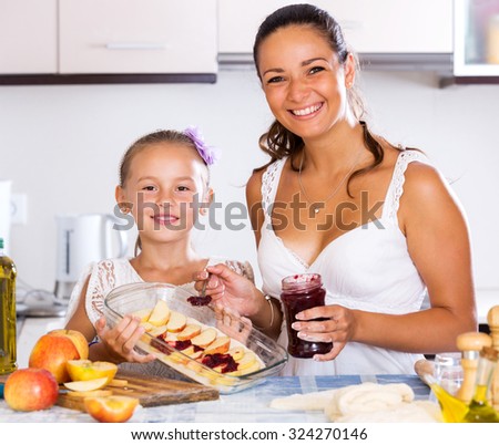 Positive little daughter helping mom to make apple cake at home. Focus on the girl