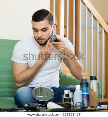 positive russian man looking at mirror and shaving beard with trimmer