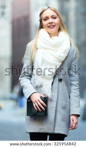 Elegant charming young blonde walking on a city street outdoors dressed in a warm coat and scarf