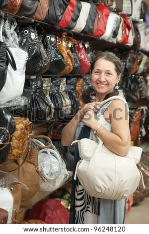 Mature woman chooses leather bag at  shop