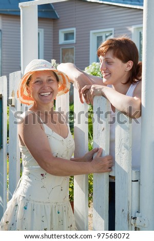 Two happy women near fence wicket  in front of home