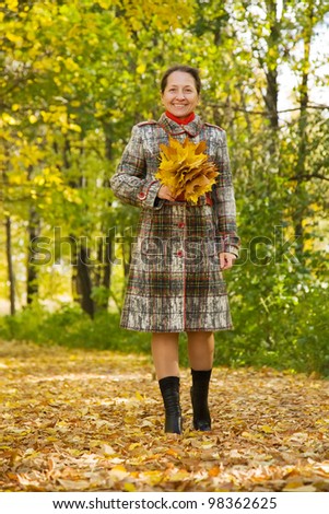 elderly woman with maple leaves walking in autumn park