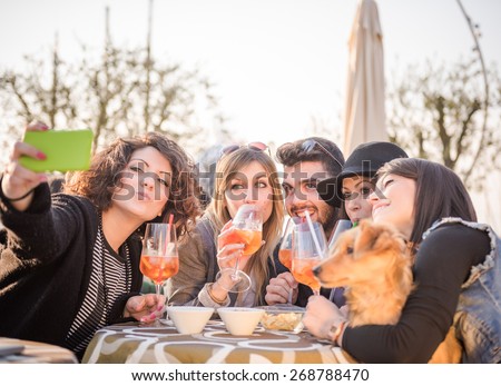 group of happy friends with smartphone taking selfie and drinking aperitif at cafe