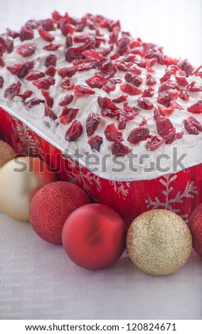 Christmas Bread With White Frosting and Cranberries in a Red Pan With Snowflakes and Christmas Ornaments