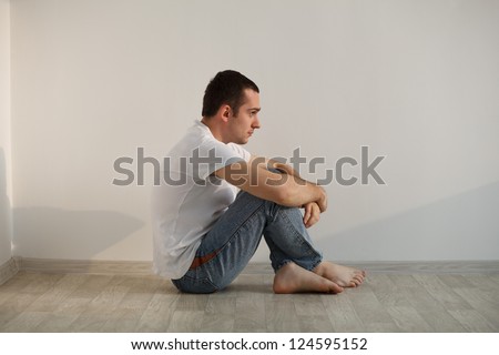 Stressed handsome young man sitting on floor, wearing white t-shirt and pants. Studio shot, natural light.