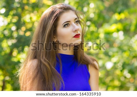 Portrait of beautiful young brunette woman with long hair wearing a blue knitted dress on a background of autumn nature