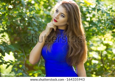 Portrait of beautiful young brunette woman with long hair wearing a blue knitted dress on a background of autumn nature