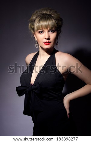 Portrait of beautiful young women exists blonde with bright makeup. Girl dressed in black evening dress on a black background.