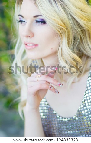Portrait of a beautiful young blonde woman with long wavy hair in shiny black dress on nature.