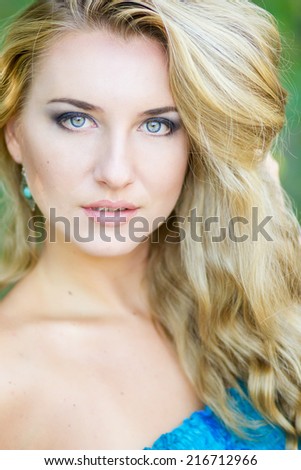 Portrait of a beautiful young blonde woman in nature. Sensual and sweet girl posing in the park on trees background