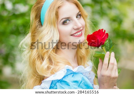 Portrait of a beautiful young blonde woman with long hair dressed as Alice in Wonderland.The girl is holding a red rose. Soft focus