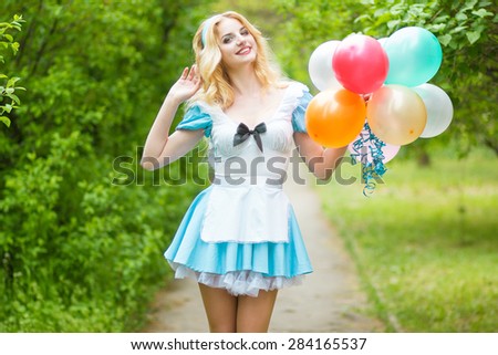 Portrait of a beautiful young blonde woman with long hair dressed as Alice in Wonderland.Girl posing with a big bunch of colorful balloons. Soft focus