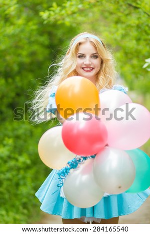 Portrait of a beautiful young blonde woman with long hair dressed as Alice in Wonderland.Girl posing with a big bunch of colorful balloons. Soft focus