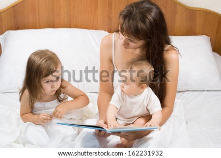 Mother reading bed time story book to daughters in bed