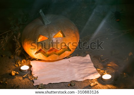 Scary Halloween pumpkin and old burned paper ad layout with candlelight and autumn leafs. Night and moon light. Still life. Wooden background.