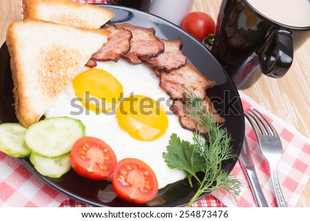 fried eggs with bacon, bread, coffee and vegetables on black dish